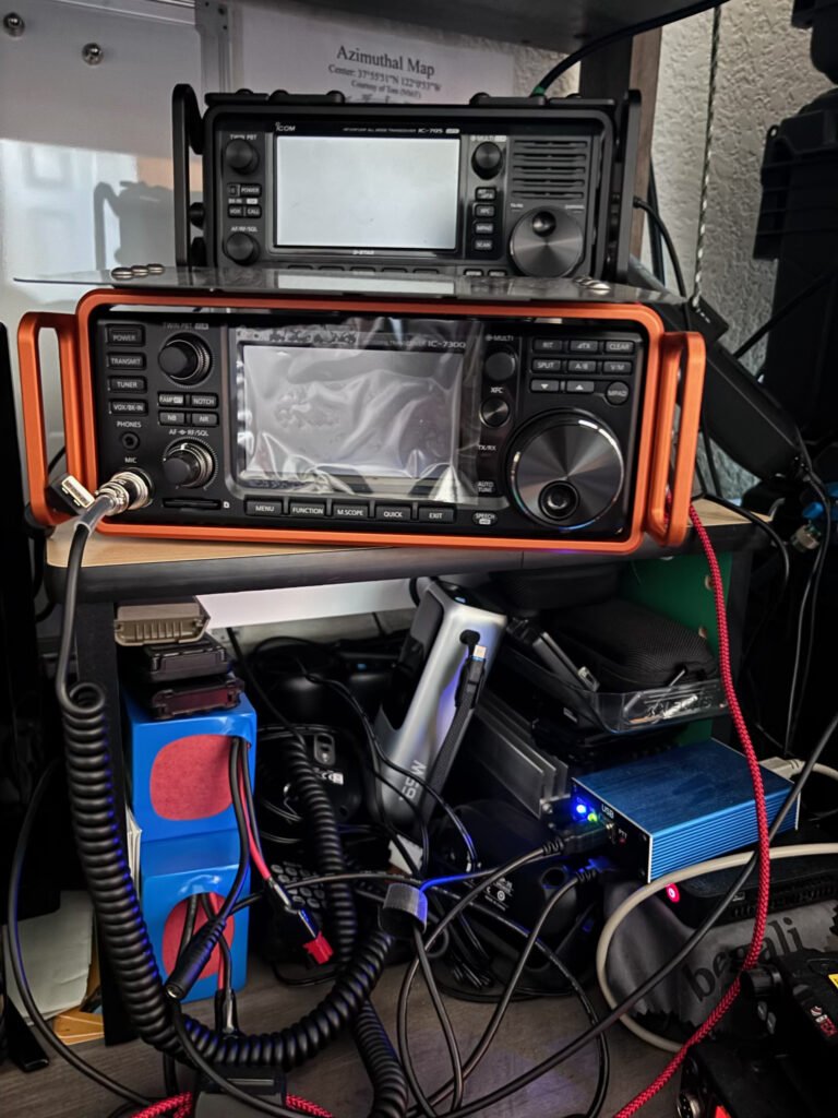 multiple radios sitting on a shelf with various other electronic equipment strewn about